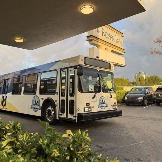 Universal Partner Hotel shuttle bus parked outside the Rosen Inn Closest to Universal, under a cloudy sky during sunset hours