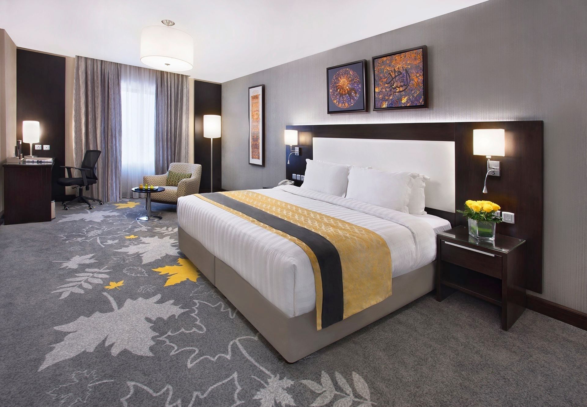 Work desk, nightstand, and cozy lounge chair by the bed in the Deluxe Room with carpeted floors at Warwick Hotel Jeddah