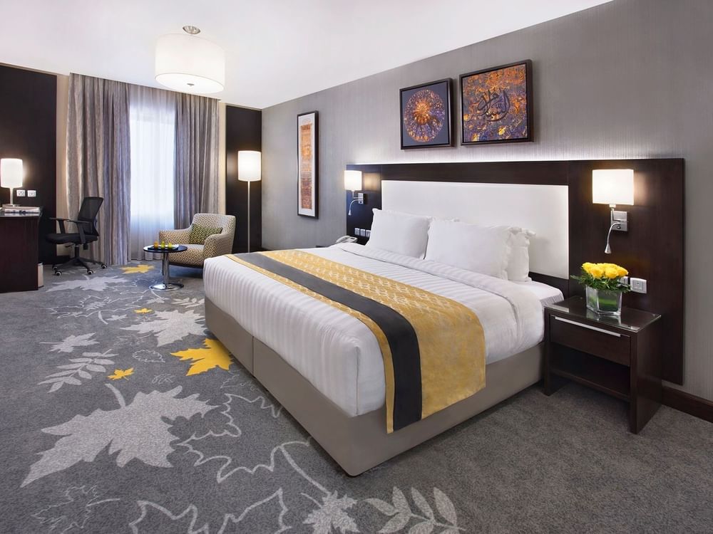 Work desk, nightstand, and cozy lounge chair by the bed in the Deluxe Room with carpeted floors at Warwick Hotel Jeddah