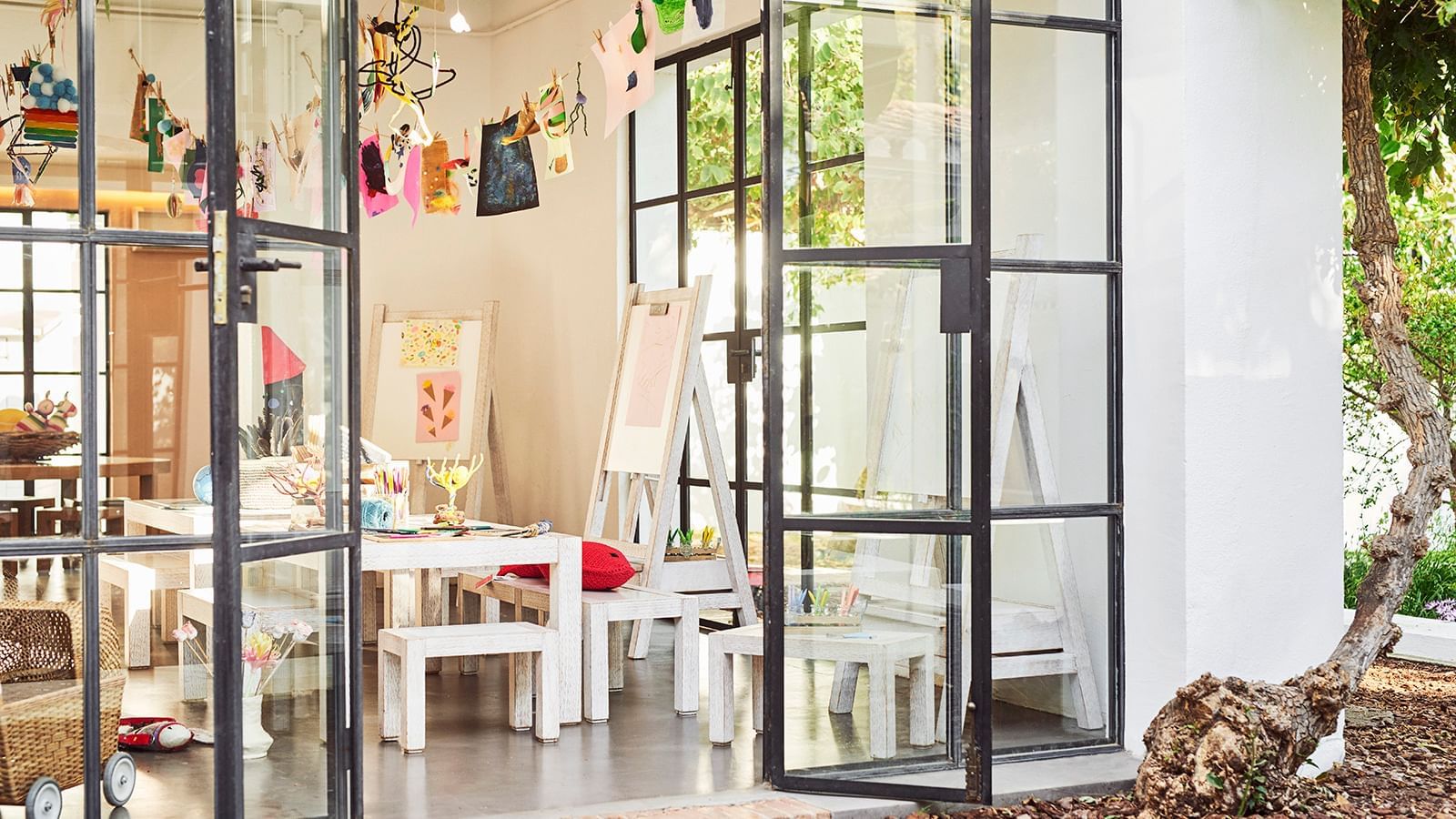 Kids' club art room with easels and small white tables placed near glass doors at the Marbella Club