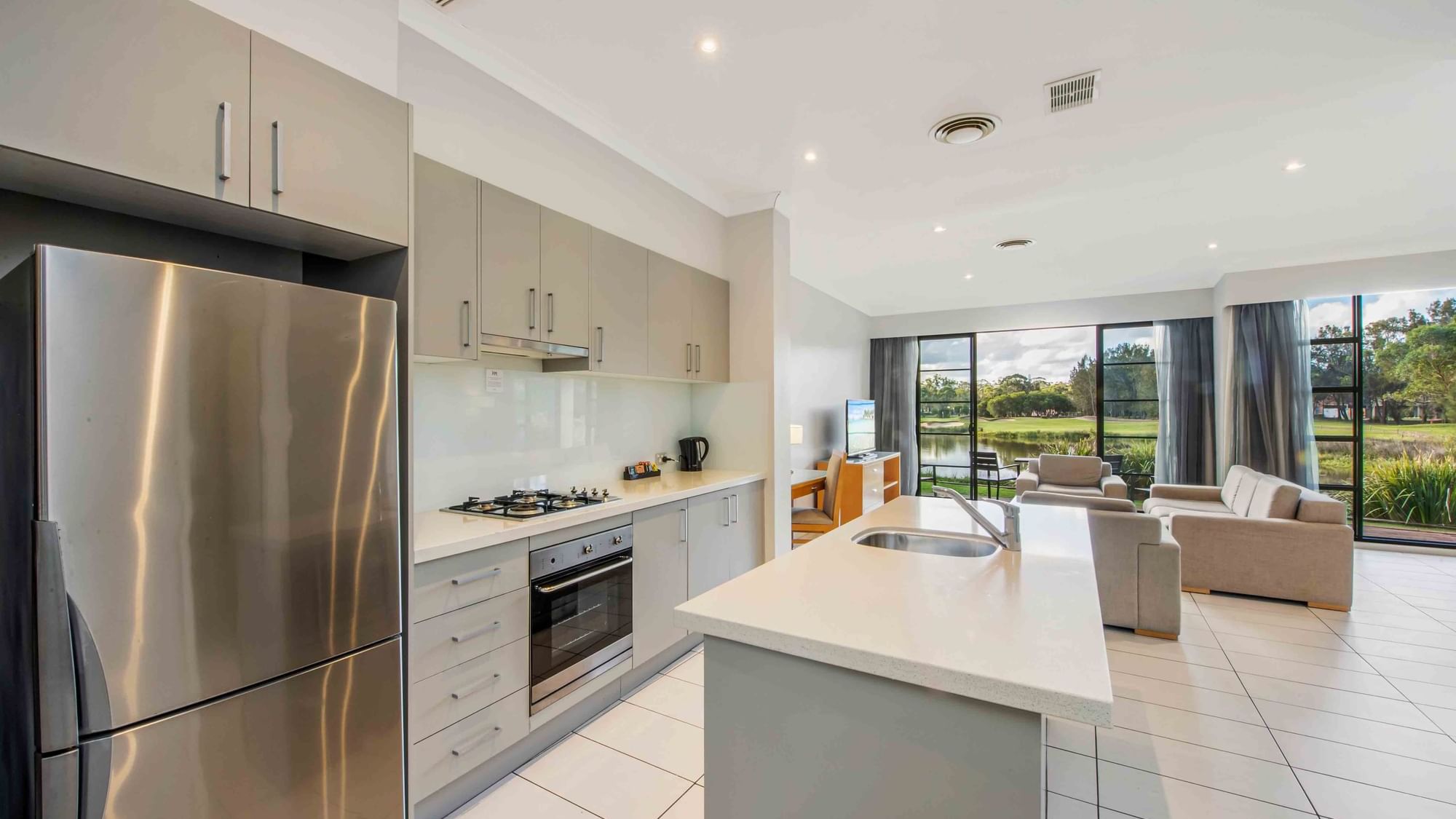 Three Bedroom Apartment kitchen with fridge and island, leading to a living room at Mercure Kooindah Waters