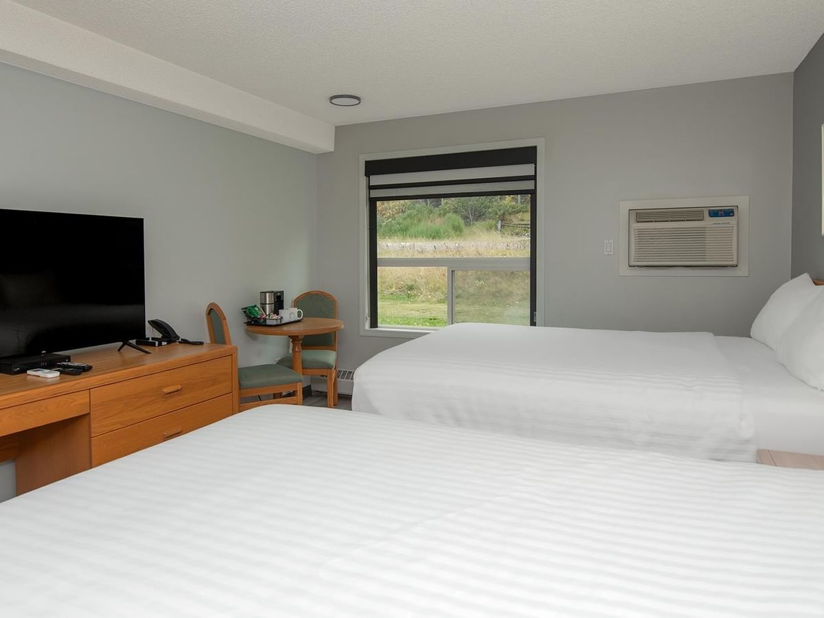 Two queen beds with white linens, wooden dresser with TV, and window with natural light.