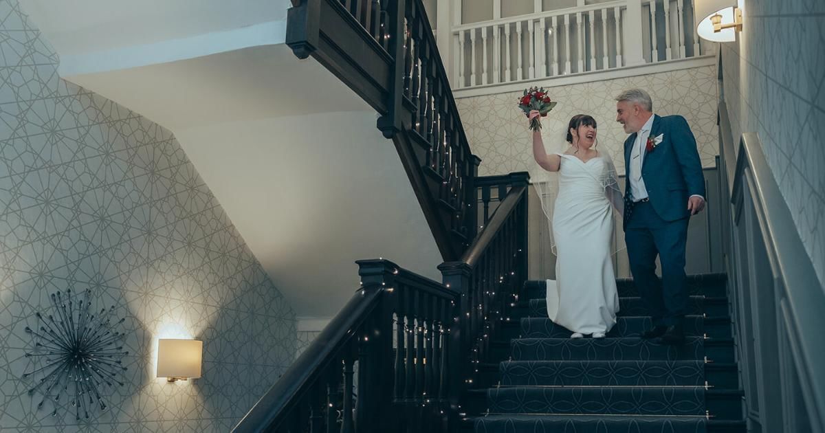 Bride and groom walking down grand ballroom staircase at Villiers Hotel in Buckingham