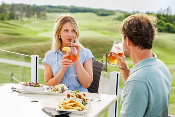 Man & woman drinking cocktails and beer while dining on an outdoor patio at Rodd Crowbush Golf & Beach Resort