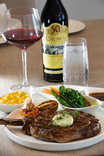 Grilled steak, vegetables, wine, and water on table at Ellipse Grace Bay