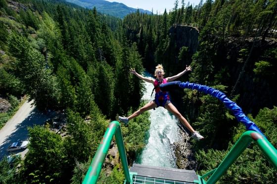 Woman bungee jumping over a river surrounded by dense forest at Aava Whistler