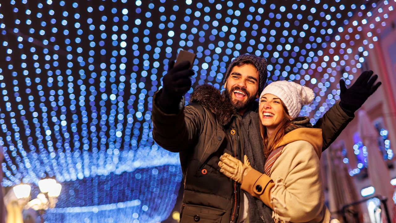 A couple taking a selfie under a blue light canopy in an outdoor setting.