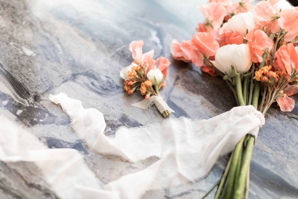 Elegant peach and white wedding bouquet and boutonnière on a marbled surface at El Prado Hotel