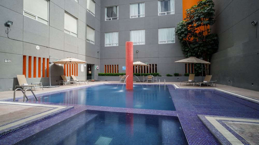 Refreshing outdoor pool featuring a central water fountain and shaded lounge chair areas at Real Inn Torreon
