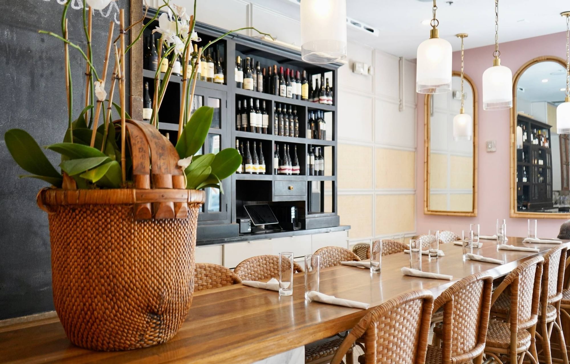 A dining area with a wooden table and chairs, a wine cabinet, and a wicker basket with plants.