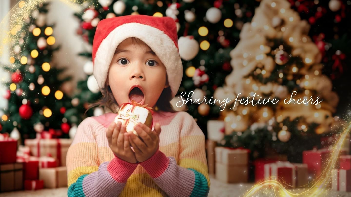 A child in a Santa hat holds a gift with mouth open, in front of decorated Christmas trees.