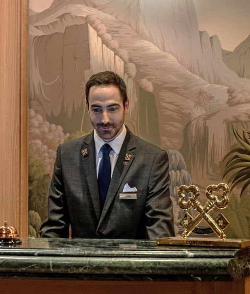 Concierge standing by a marble desk and a golden statue in a niche at the lobby of Hotel Westminster Paris