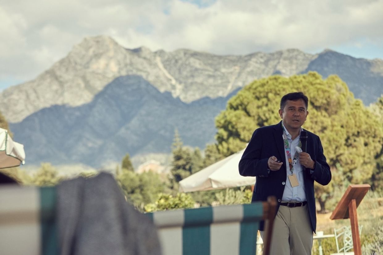 Speaker at a lectern with La Concha mountain and cloudy skies in the background near Marbella Club