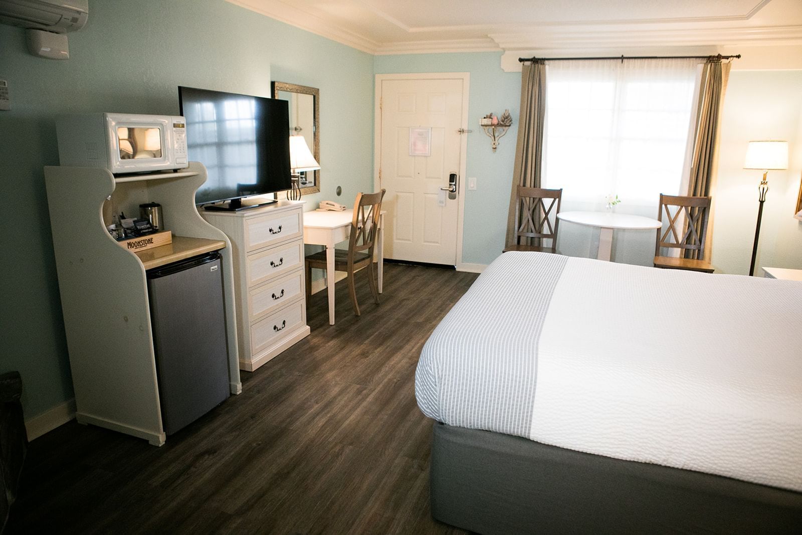A hotel room with a king-sized bed, desk, refrigerator, microwave, and flat-screen TV.