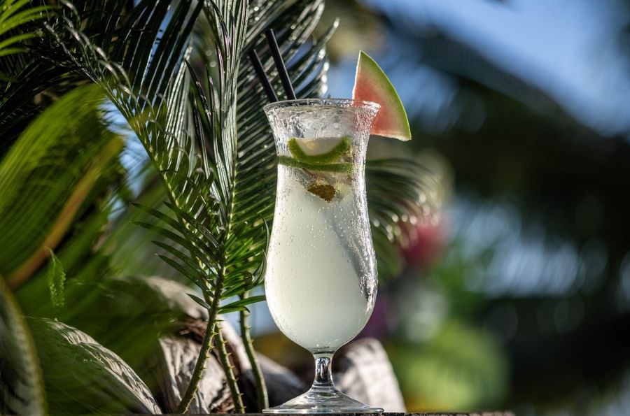Cold cocktail with a lime slice by green palm leaves in Sunset Terrace Bar at Warwick Fiji Resort and Spa