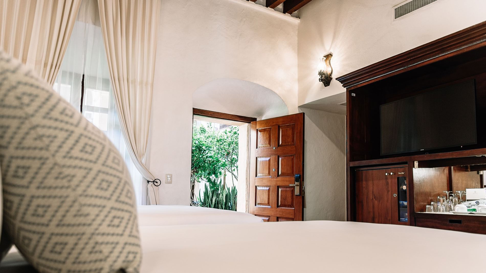 Elegant wooden furniture with glassware and a TV by the bed in 2 Double Superior Suite at Quinta Real Oaxaca
