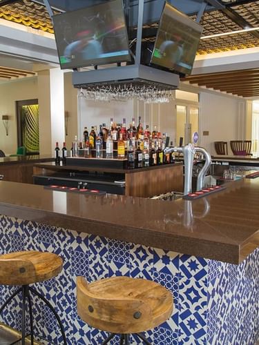 Wooden stools by a blue patterned bar and TV monitors in Rum Cay Lobby Bar at Warwick Paradise Island Bahamas