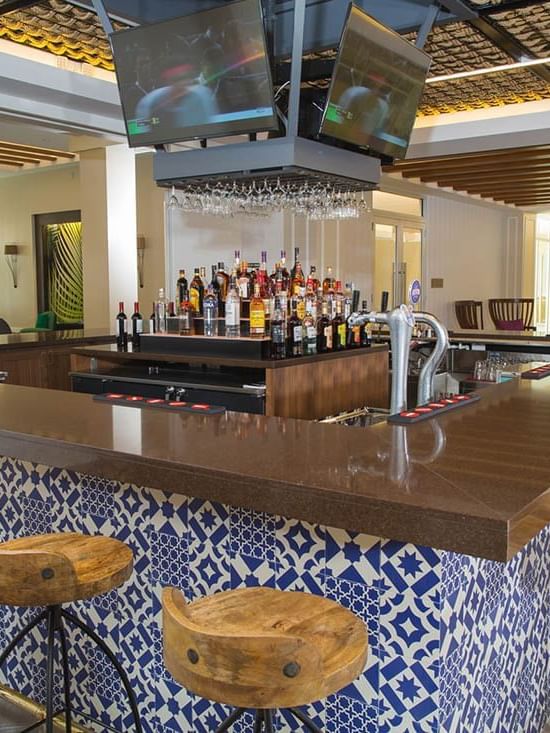 Wooden stools by a blue patterned bar and TV monitors in Rum Cay Lobby Bar at Warwick Paradise Island Bahamas