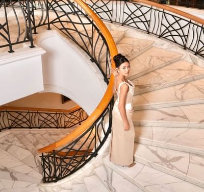 Woman standing on a marble staircase with a wooden and black wrought iron railing at Hanoi Daewoo Hotel