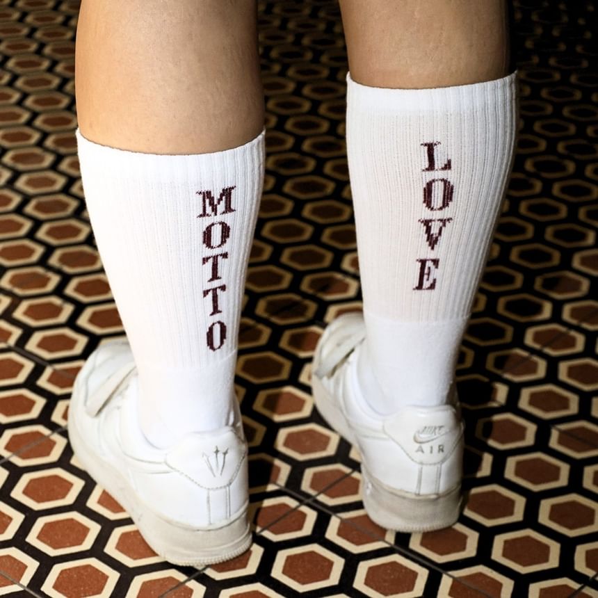 weiße Socken mit MOTTO und LOVE Schriftzug und weißen Turnschuhen auf gemustertem Boden vom Hotel Motto Wien