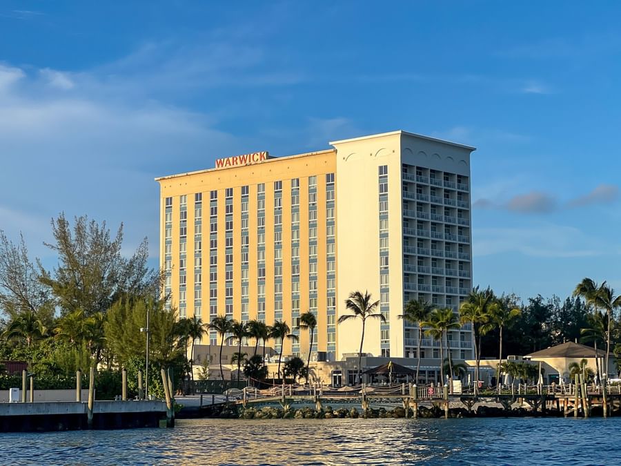 High-rise resort by palm trees and a wooden pier under a soft blue sky near Warwick Paradise Island Bahamas