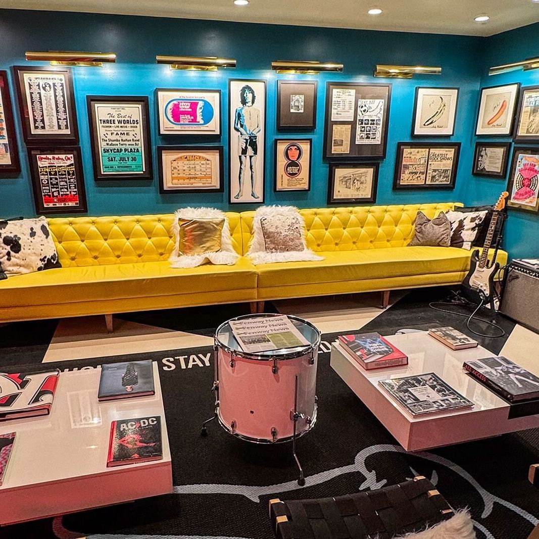 Vibrant music-themed lounge with yellow tufted sofa, vintage concert posters, guitars, and drum against turquoise walls