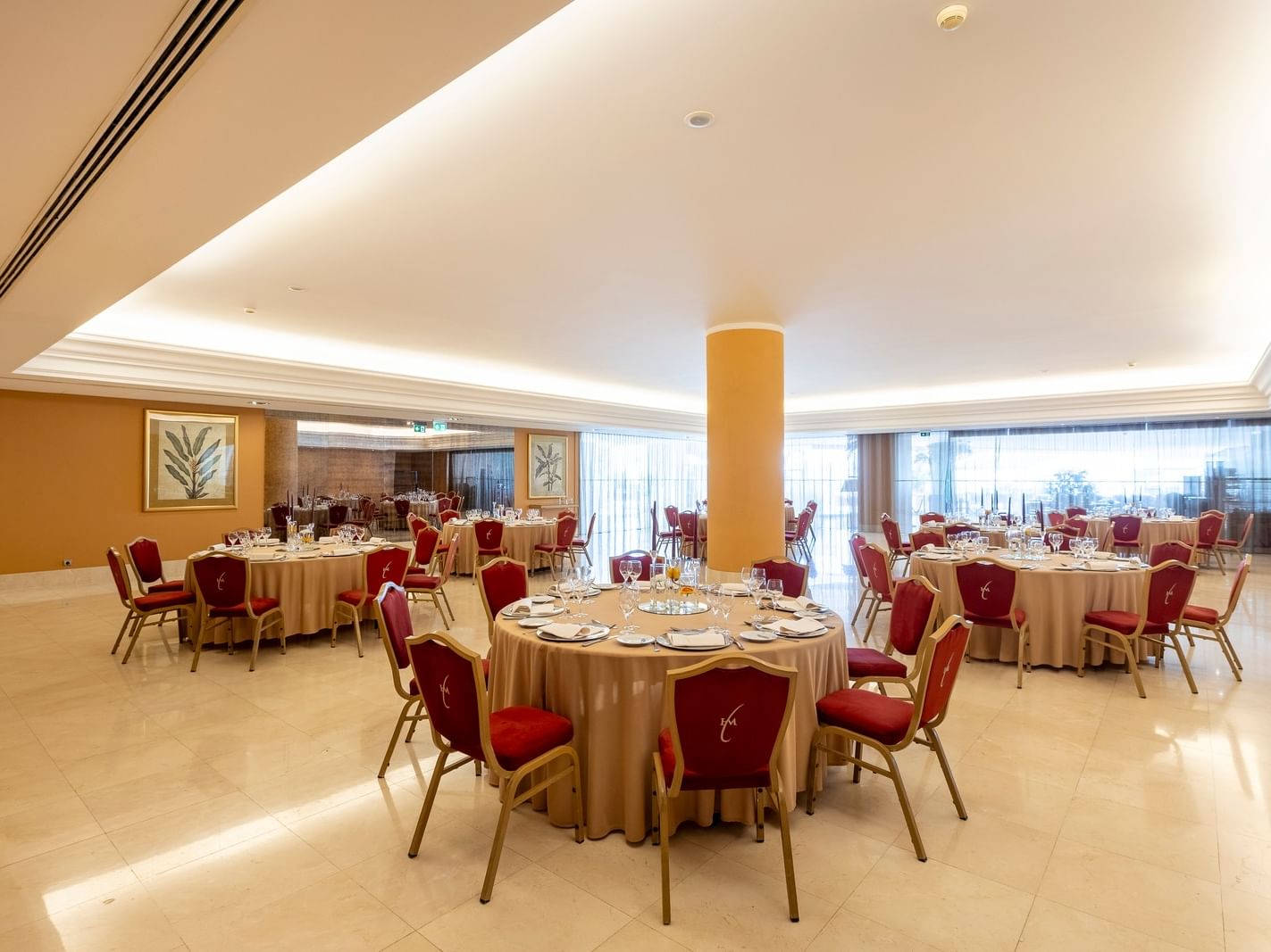 Comedor elegante con mesas redondas cubiertas de tela y sillas rojas, en un espacio bien iluminado.