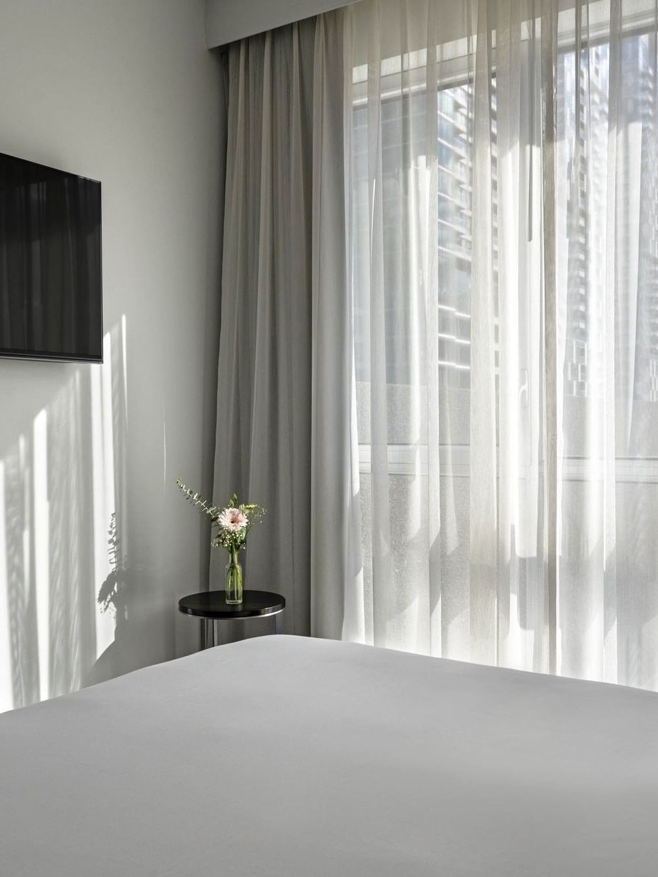 White bed with TV, curtains, and flowers near window in Penthouse René-Lévesque at Warwick Le Crystal Montreal.
