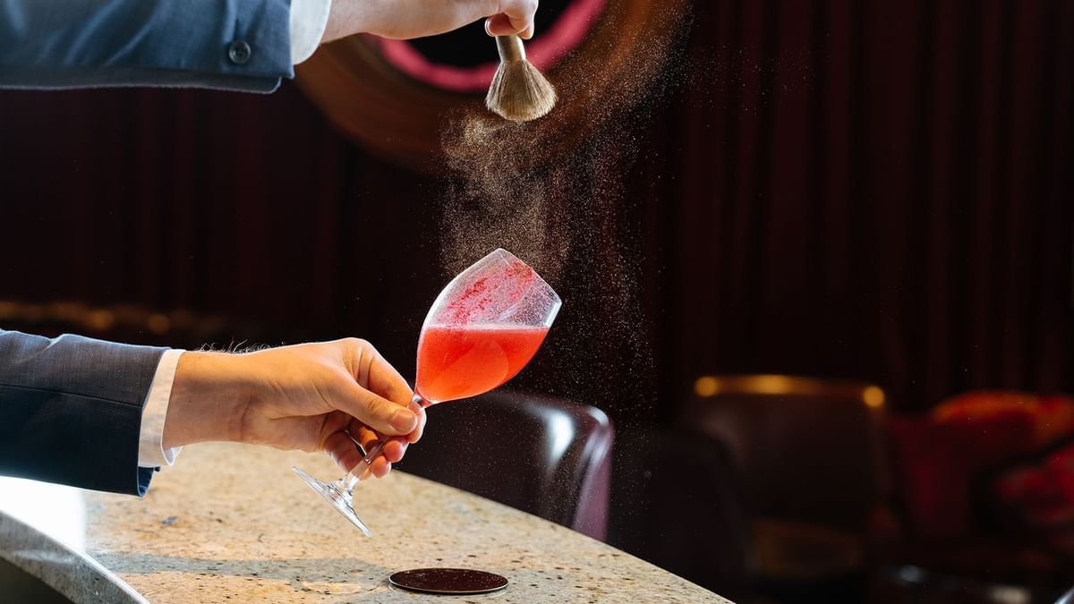 Person sprinkling spices over a red cocktail in a La Vie Champagne Lounge at Crown Hotels