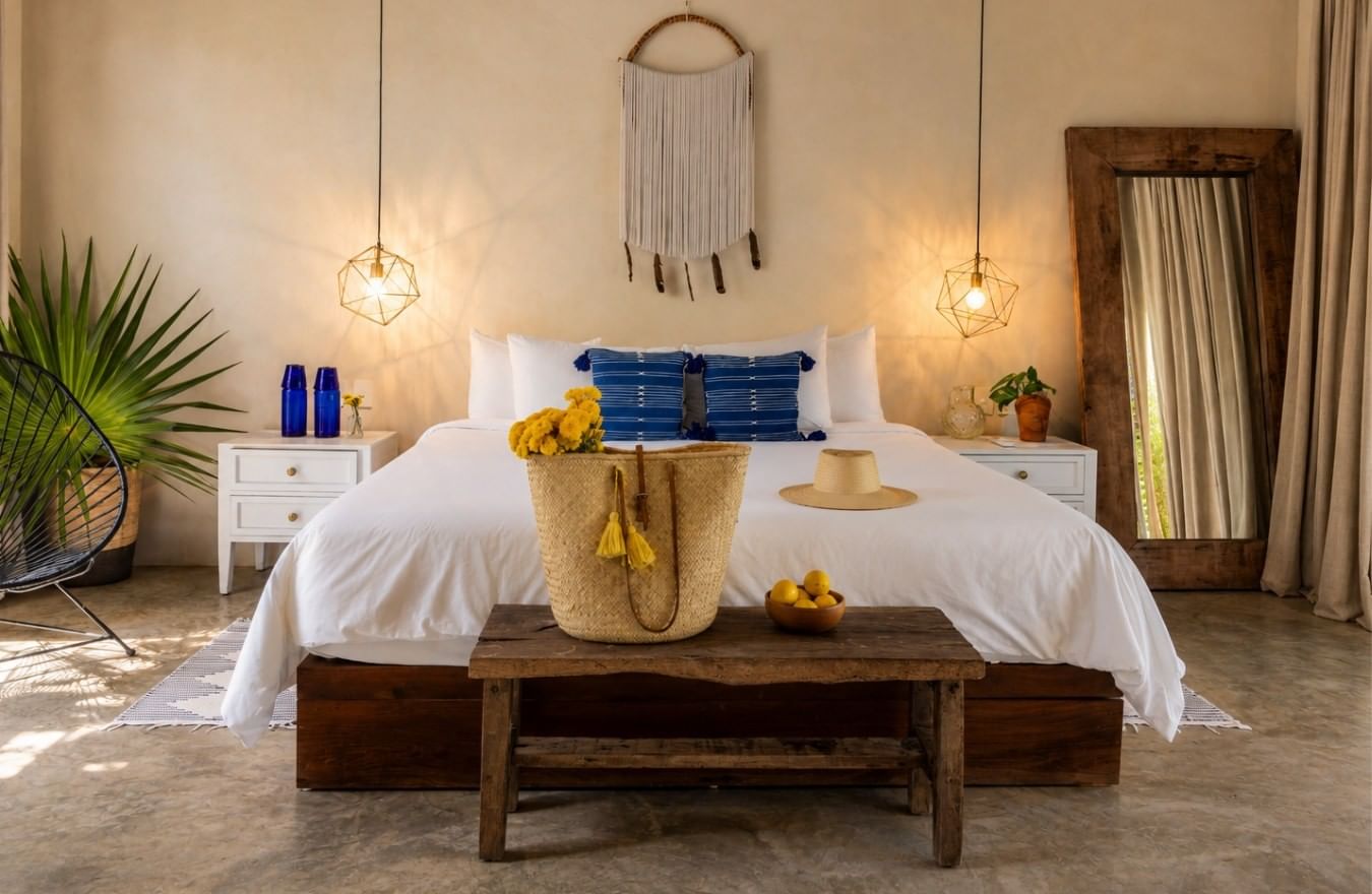 A La Zebra beachside suite with white bedding, indigo cushions, natural finishes and a woven beach bag.