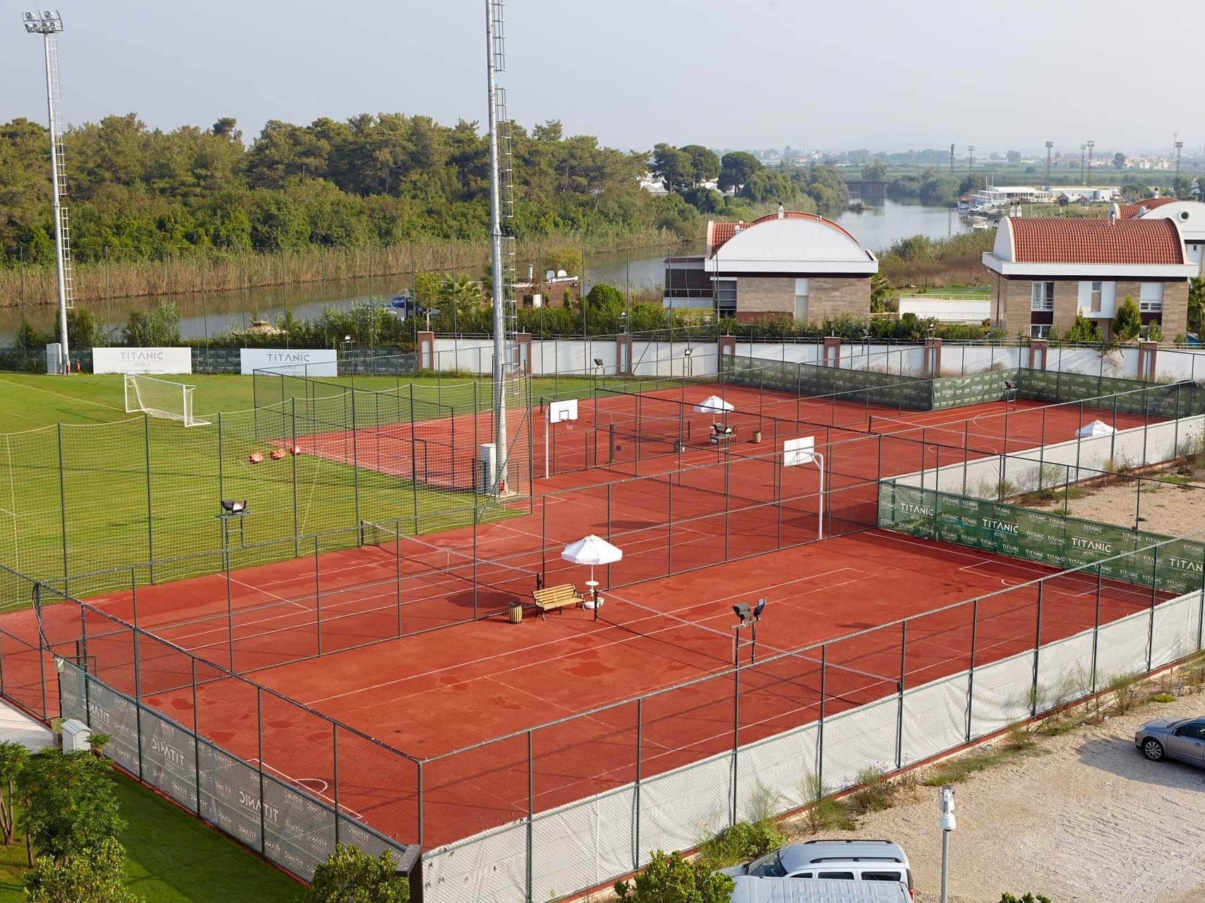 High-angle view of tennis court surrounded by fencing with adjacent soccer field at Titanic Deluxe Golf Belek