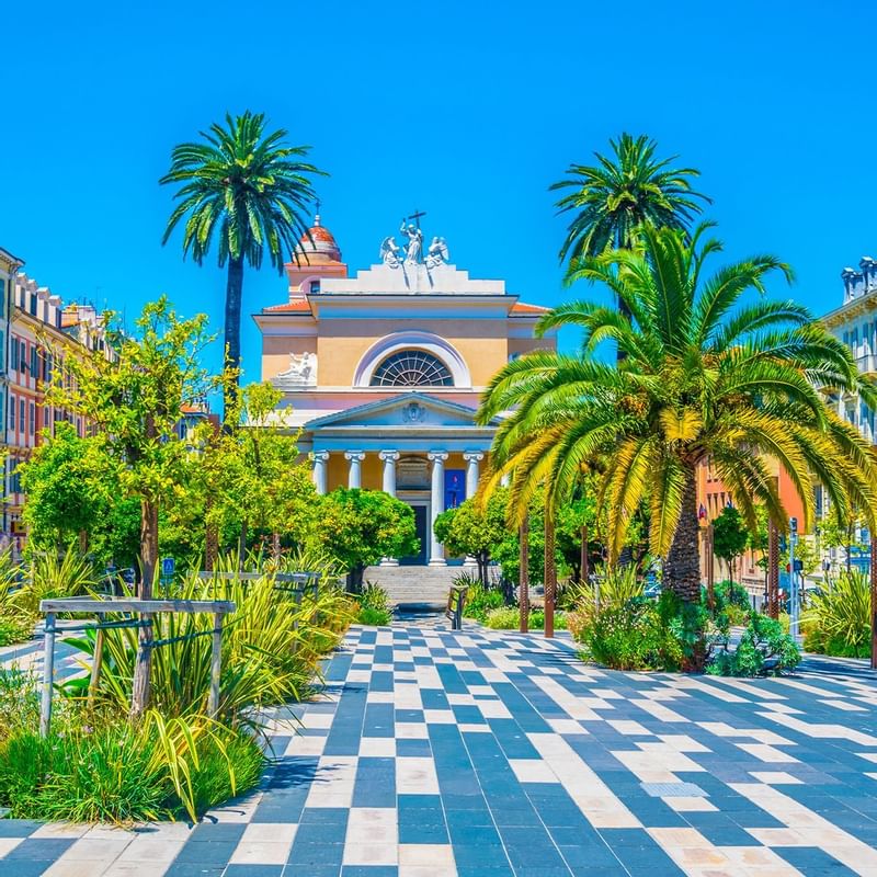 Vibrant plaza with palm trees, greenery, and a historic building in Nice near Warwick Hotels and Resorts