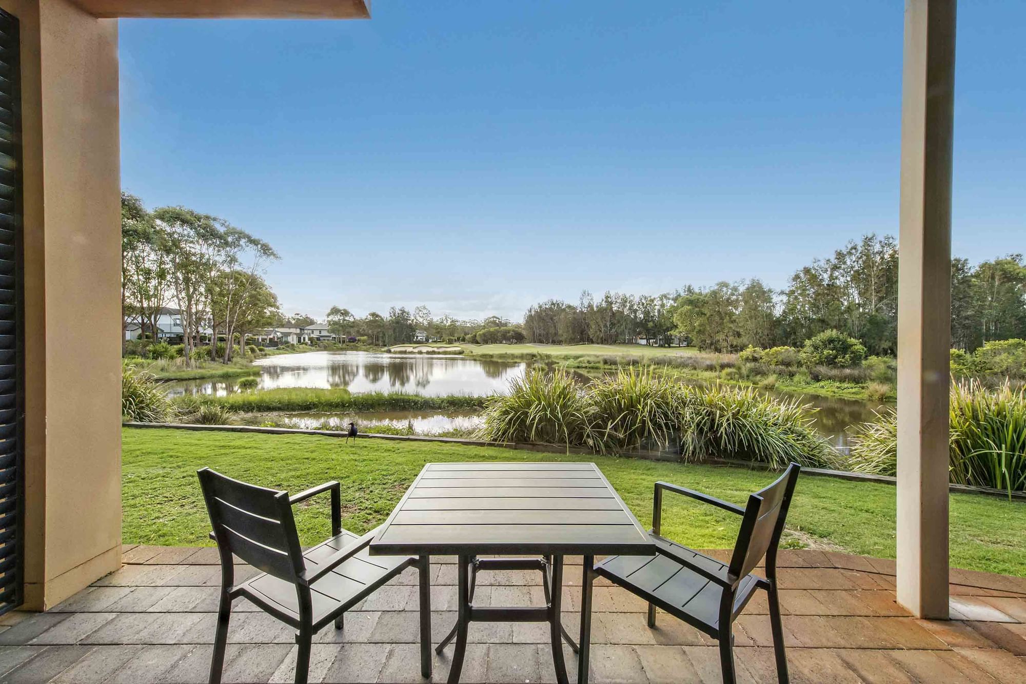 Patio with table and chairs overlooking a lake and lawn at Mercure Kooindah Waters