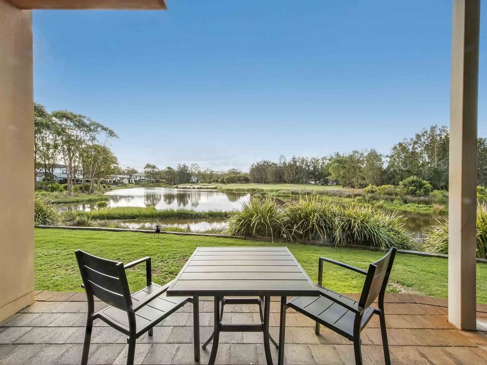 Patio view with a table and chairs overlooking a serene pond and green landscape at Mercure Kooindah Waters