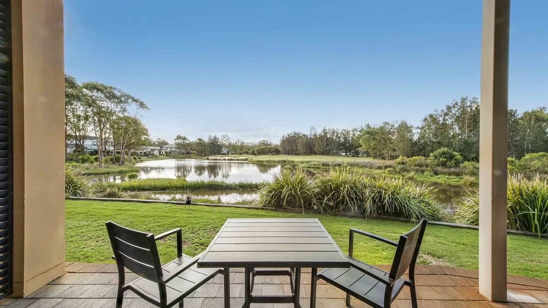 Patio view with a table and chairs overlooking a serene pond and green landscape at Mercure Kooindah Waters