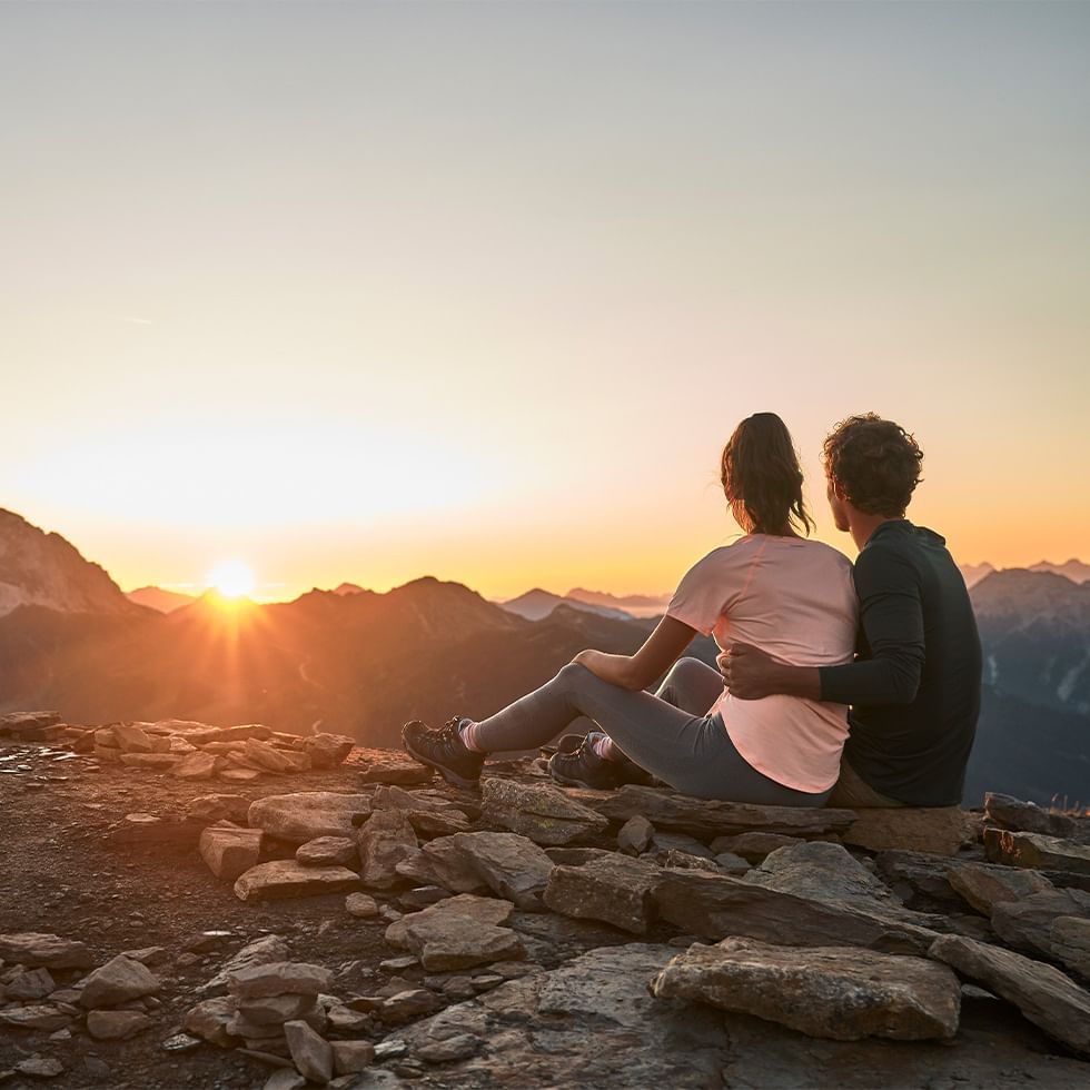 Couple sitting on a mountain at sunset, overlooking a range of peaks near Falkensteiner Hotel Antholz