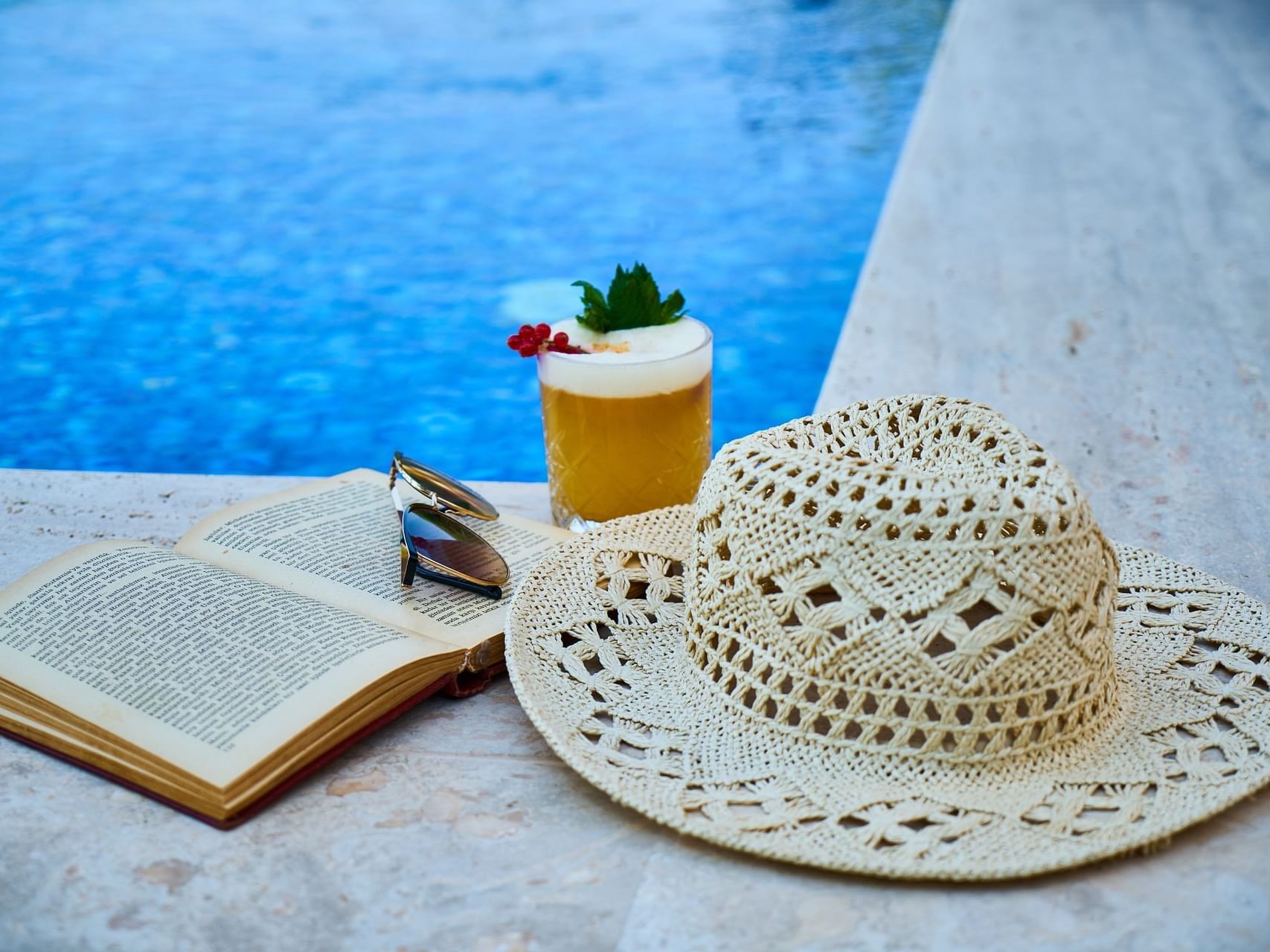 A Hat, book, & a drink on the pool corner at Bay Club Hotel