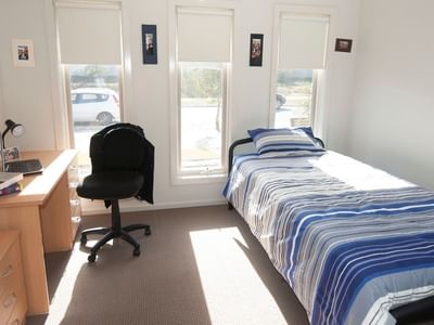 Bedroom with bed, desk, chair, and window at La Trobe University Regional Housing.