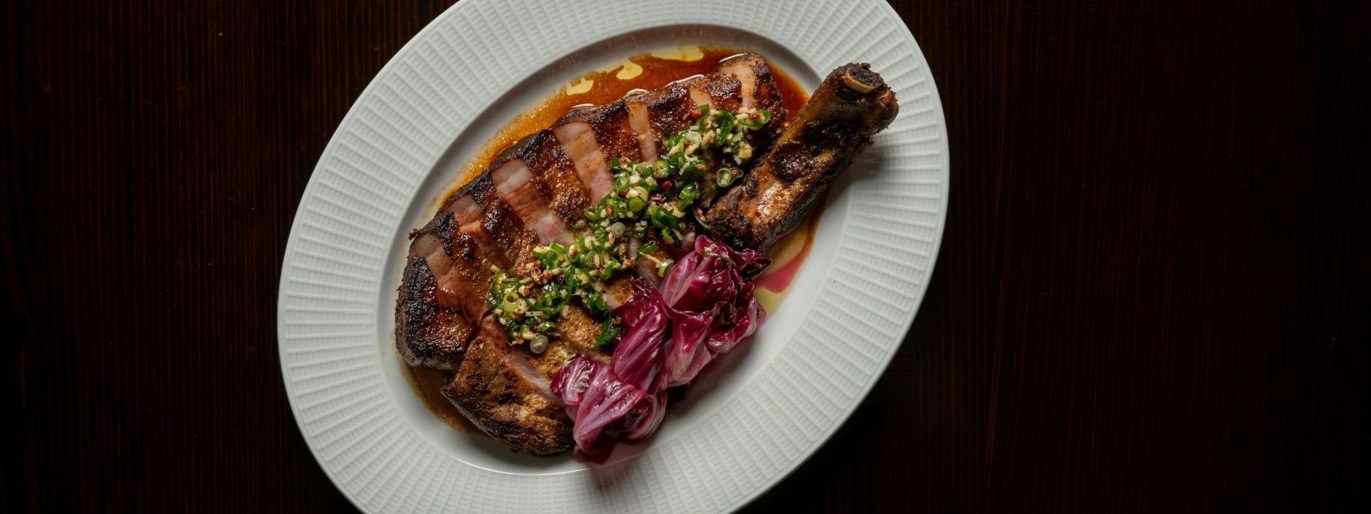 Grilled steak with herb topping and pickled onions on a white plate for NRL Grand Final Dining