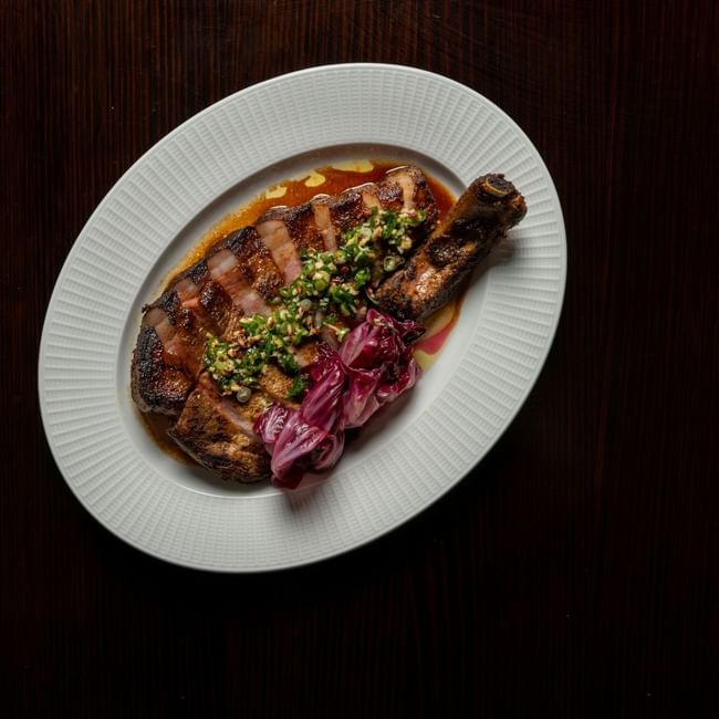 Grilled steak with herb topping and pickled onions on a white plate for NRL Grand Final Dining