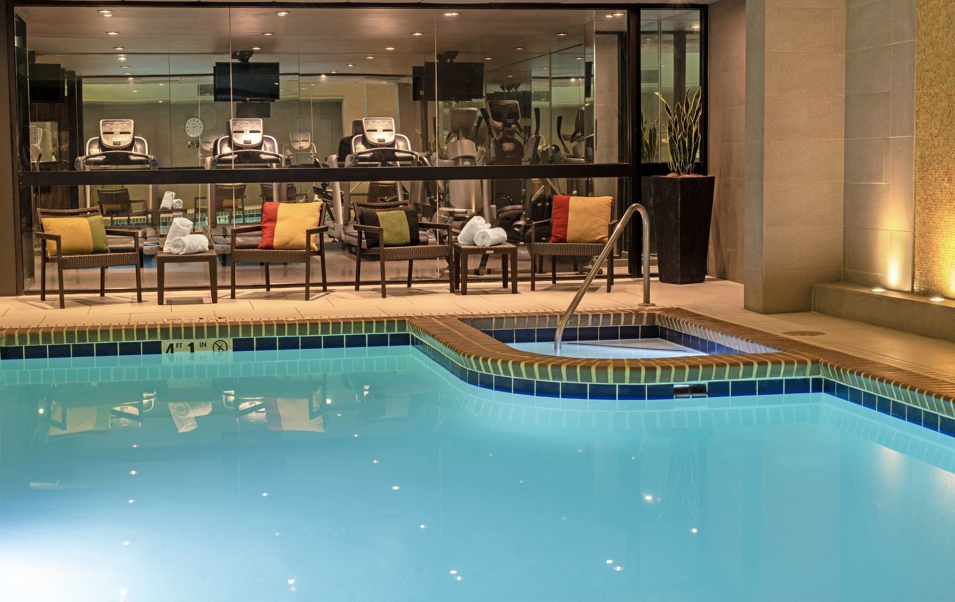 Indoor pool and hot tub by lounge chairs under a glass wall at Warwick Seattle