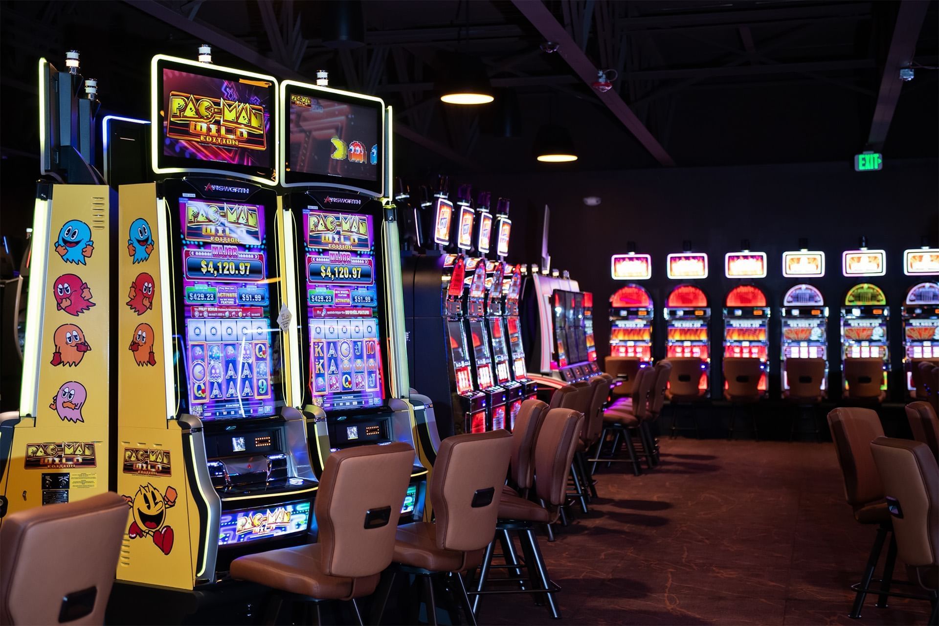 Row of Casino Gaming machines with brown leather chairs, under ceiling lights, in a dim casino aisle at The Brook