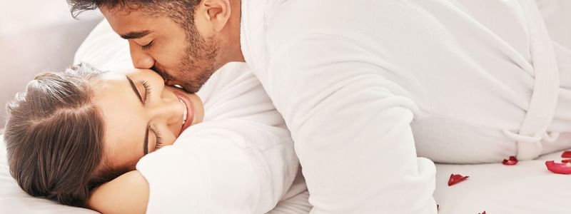 Couple in bathrobes sharing a tender moment on a bed with rose petals, promoting the Soulful Harmony treatment.