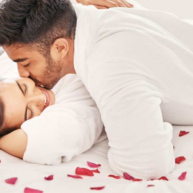 Couple in bathrobes sharing a tender moment on a bed with rose petals, promoting the Soulful Harmony treatment.