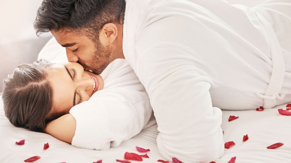 Couple in bathrobes sharing a tender moment on a bed with rose petals, promoting the Soulful Harmony treatment.