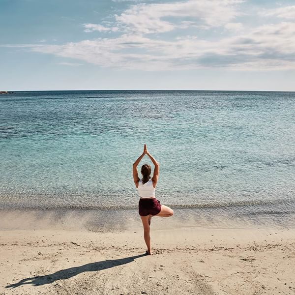 Person practicing yoga on a tranquil beach, clear skies above near the Falkensteiner Hotels & Residences