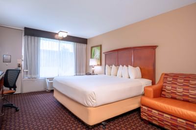 Guestroom with king bed, wooden headboard, work desk, and occasional chair at Rosen Inn International