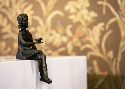 A bronze sculpture of a seated figure against a textured floral backdrop at The Roxbury