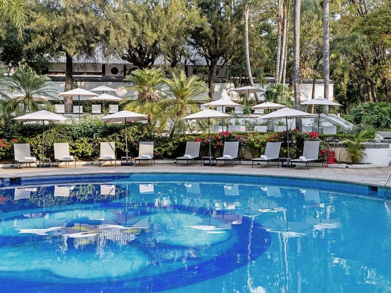 Luxurious swimming pool surrounded by lounge chairs and lush greenery at Grand Fiesta Americana