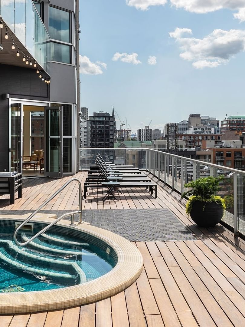 Outdoor hot tub on a wooden deck by a glass railing, under string lights at Warwick Le Crystal Montreal